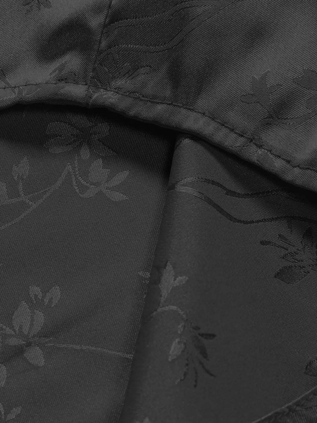 Close-up of black fabric with a subtle floral and vine jacquard pattern, perfect for men's summer shirts. The image highlights stitching, folds, and sheen, showcasing the breathable fabric’s texture and elegant details.