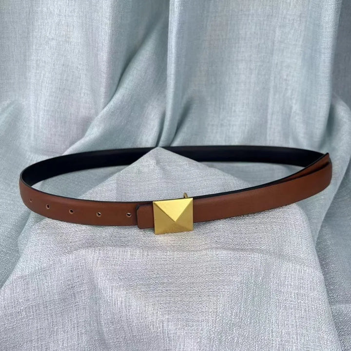 A brown leather belt with a large, square gold buckle and adjustable length is displayed on a light gray textured fabric background.