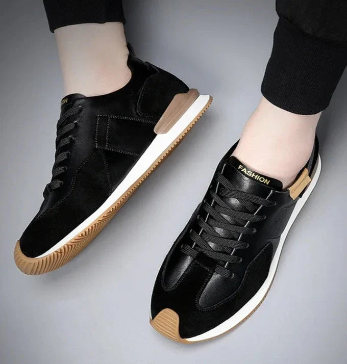 A person wearing black sneakers with white soles, brown toe caps, and the word FASHION printed on the tongue, shown from above against a light gray background. These shoes offer arch support for enhanced comfort.