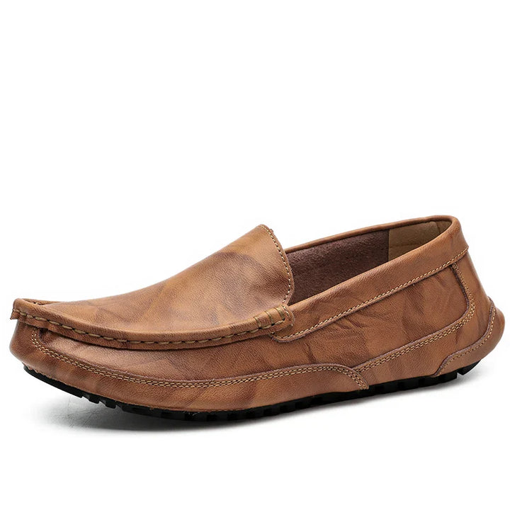 A single hand-stitched moccasin brown leather loafer with visible stitching, a rounded toe, and a textured black rubber sole, displayed on a white background.