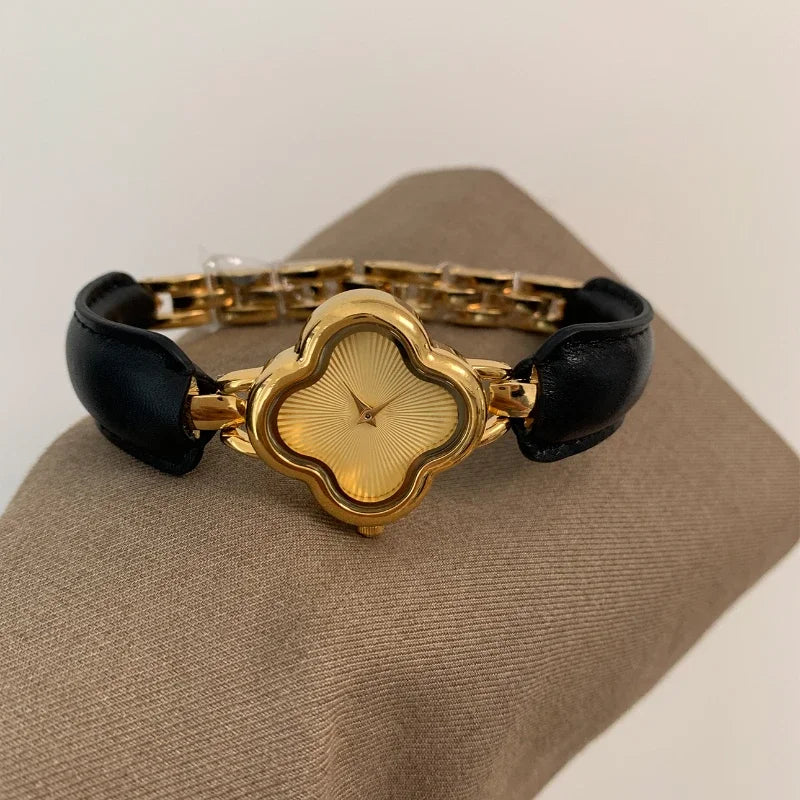 A luxury gold-plated clover dial watch with a textured yellow face, genuine leather strap, and gold bracelet links, elegantly displayed on a beige surface.