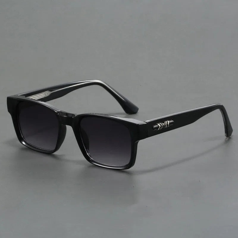 Black rectangular sunglasses with thick, durable frames and dark lenses, featuring a small silver decorative detail on the arms. Boasting UV400 protection and modern design, theyre displayed on a plain grey background.