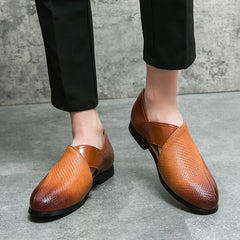 A person wears genuine leather loafers with textured detail, durable outsole, and black soles, standing on a gray concrete floor. They are dressed in black pants.