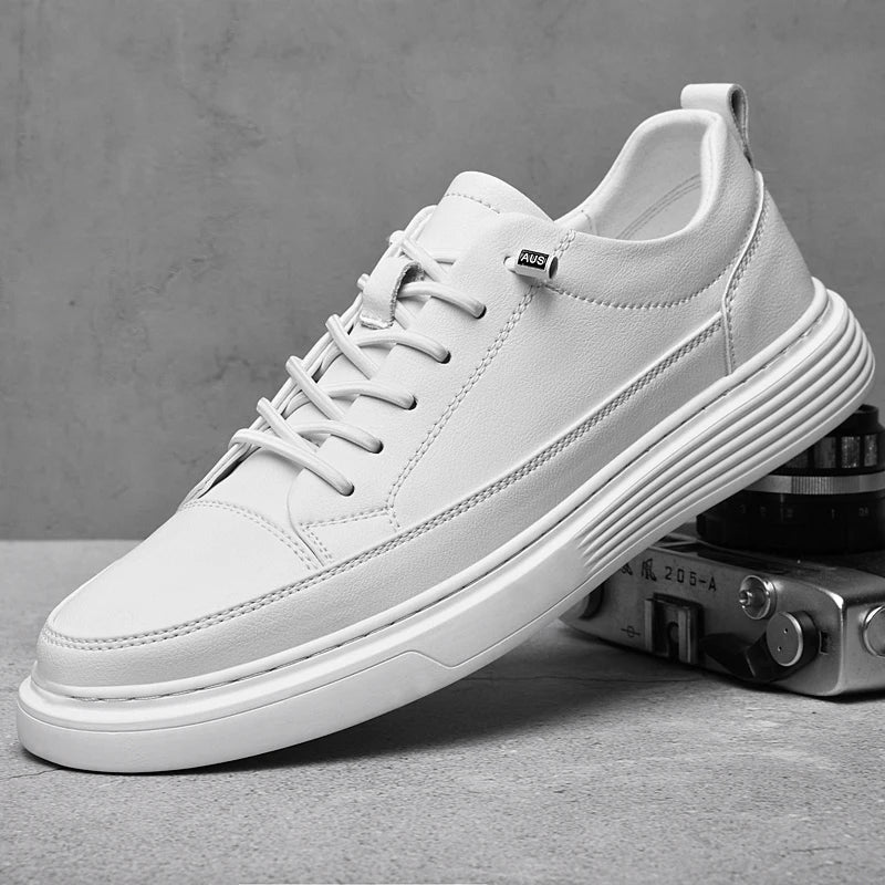 A white sneaker with a thick sole sits on a gray surface, partially resting on a vintage camera. Crafted from genuine leather, the shoe features white laces, a subtle tag on the side, and a minimalist, modern design.
