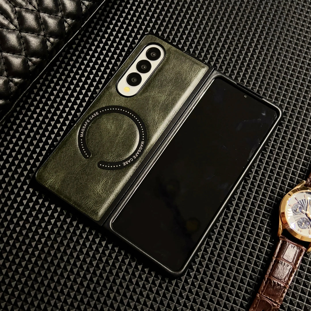 A foldable smartphone in a green Samsung Galaxy Z Fold case with circular MagSafe markings lies partially open on a textured black surface, next to a brown leather-strap wristwatch.