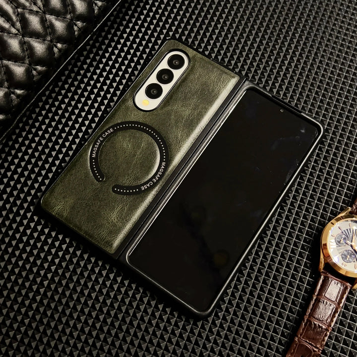 A foldable smartphone in a green Samsung Galaxy Z Fold case with circular MagSafe markings lies partially open on a textured black surface, next to a brown leather-strap wristwatch.