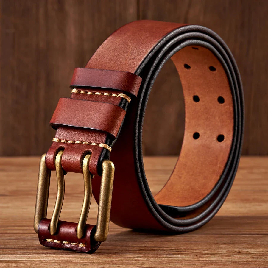 A rolled-up durable cowhide leather belt with double copper buckles and matching belt loops, placed on a wooden surface with a wooden background.