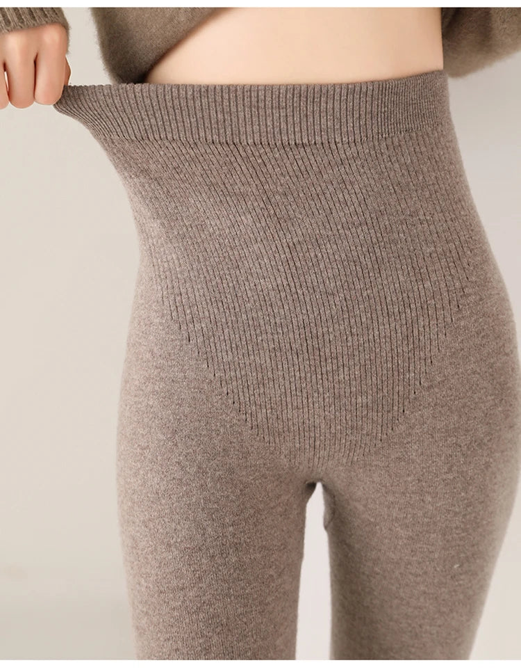 A close-up of a person wearing high-waisted, ribbed, light brown breathable knit leggings, stretching the waistband outward to show its elasticity. Only the lower torso and upper legs are visible.