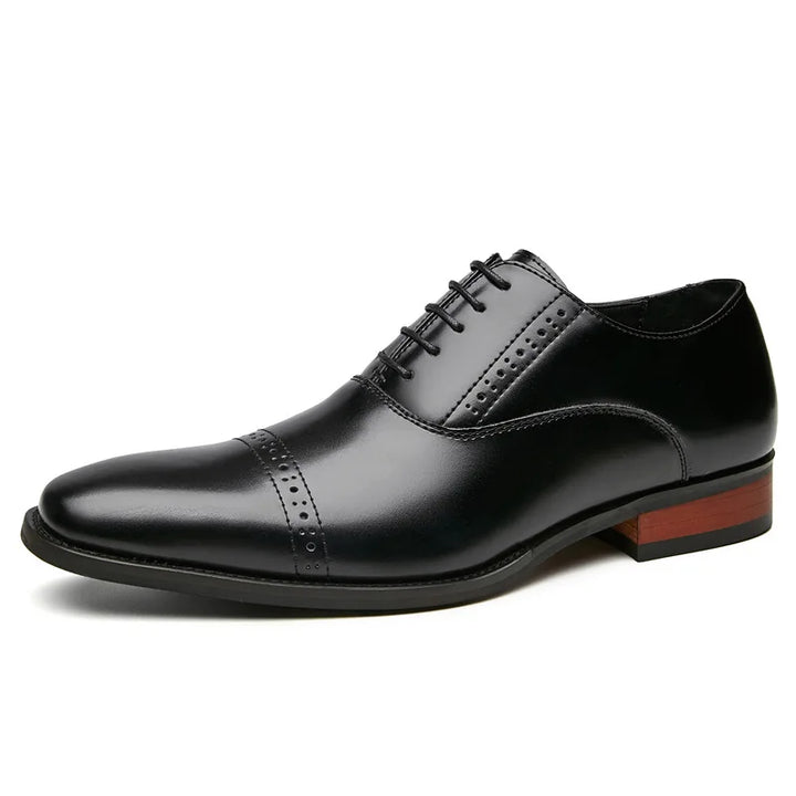 A black Italian leather oxford dress shoe with hand-stitched detailing, decorative broguing on the toe cap and sides, a closed lacing system, and a low-profile wooden heel.