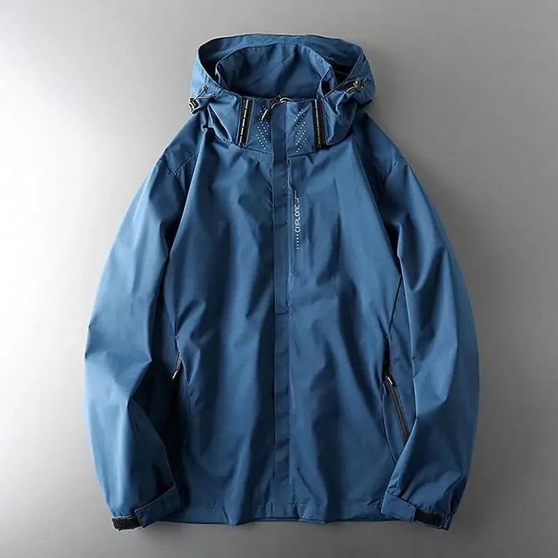 A blue hooded waterproof jacket with a front zipper, black zipper pockets on both sides, and drawstrings on the hood, laid flat on a gray surface—perfect as a windproof jacket for outdoor adventures.
