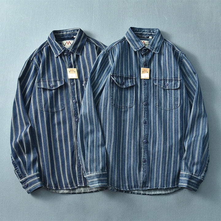 Two blue denim vintage button-up shirts with white vertical stripes and chest pockets are laid flat side by side on a light blue surface. Both feature tags attached to the collar and a relaxed fit for added comfort.