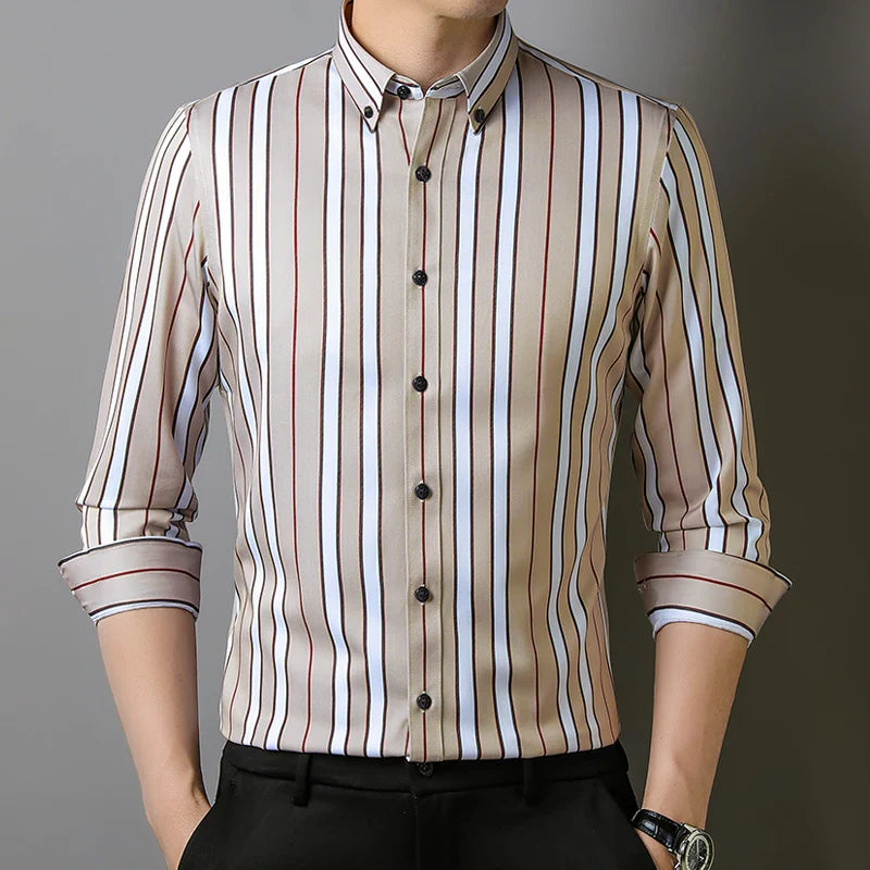 A man wears the Hamilton Executive Classic Fit Shirt—a beige button-up with vertical black, white, and red stripes. The sleeves are rolled up, hands tucked in black pants, highlighting the premium fabric shirt. His face is not visible.