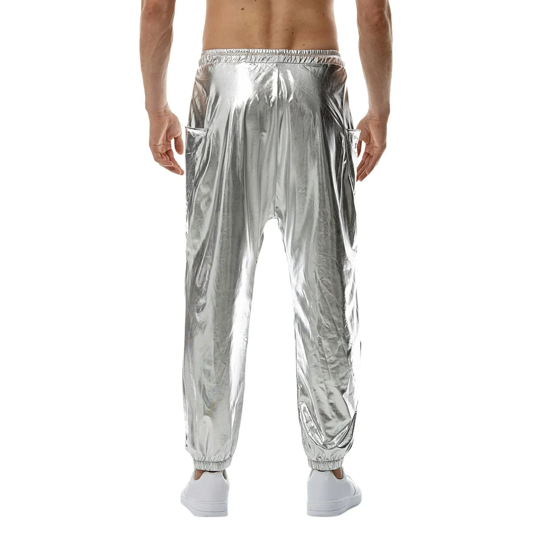 A person wearing shiny silver jogger pants made from lightweight metallic fabric with an elastic waistband and tapered leg, paired with white shoes, is shown from the back against a white background. The person is shirtless.