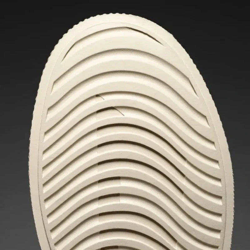 Close-up of the bottom of a beige shoe sole with a pattern of evenly spaced, curved grooves running across its durable rubber outsole. The background is plain and dark.