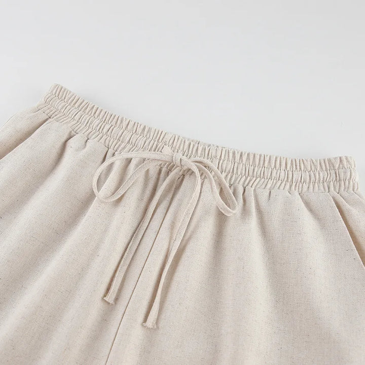 Beige wide-leg pants with an elastic waistband and side pockets, crafted in a soft Belgian Linen Blend, displayed on a flat white surface.