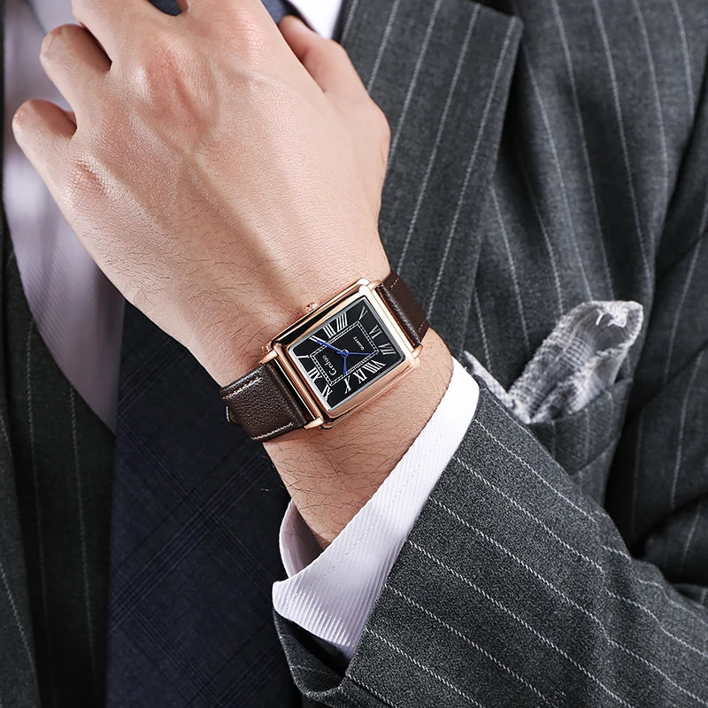 A man wearing a gray pinstripe suit and a patterned tie shows a wrist adorned with a luxury watch featuring a rectangular black face and a premium leather band.
