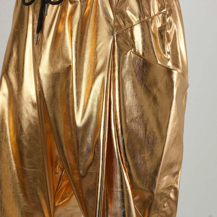 Close-up of shiny, gold metallic pants crafted from lightweight metallic fabric with a loose fit, elastic waistband, gathered waist with drawstring, and eye-catching reflective material.