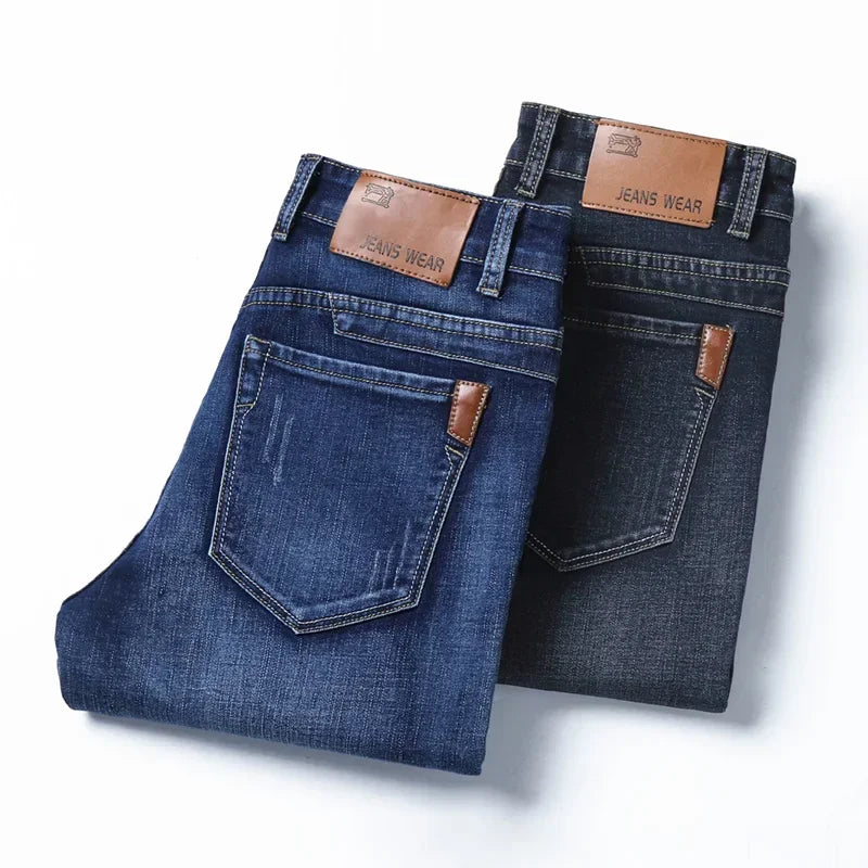Two pairs of folded slim-fit jeans, one in blue denim and the other in black, both featuring brown leather patches on the waistband and brown accents on the back pockets, crafted from durable fabric and displayed on a white background.