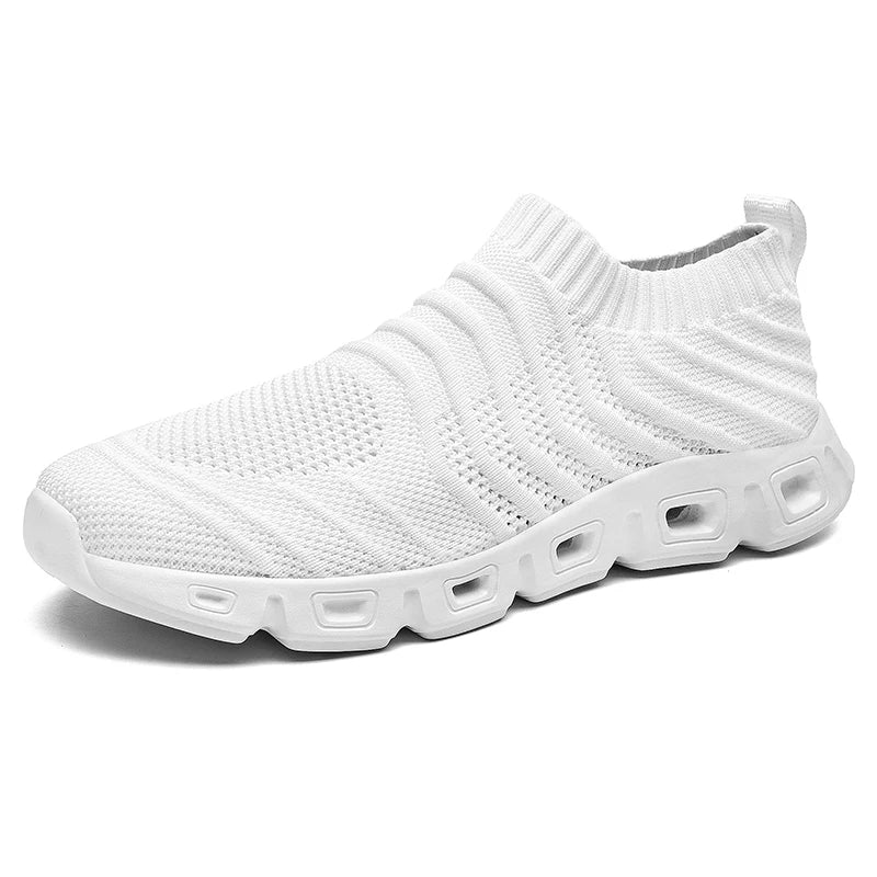A white slip-on athletic shoe with a knitted mesh upper, ribbed texture, and a cushioned sole featuring multiple rectangular cutouts along the side for comfort and support.