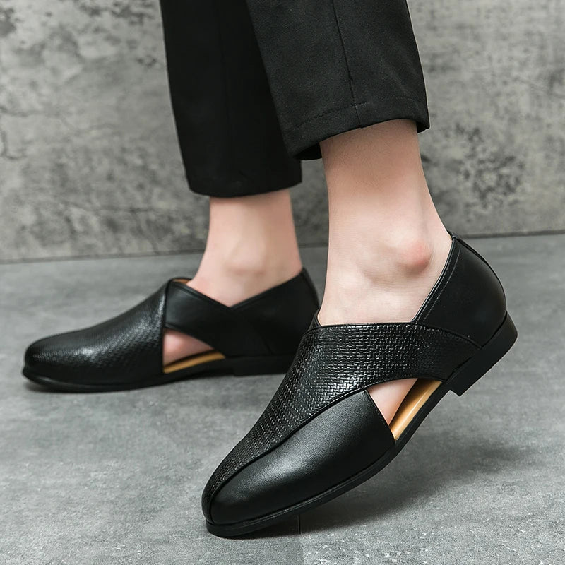 A person wearing genuine leather loafers with textured and smooth sections, featuring stylish open sides and a durable outsole. The low profile loafers are paired with black pants as the person stands on a grey tiled floor.