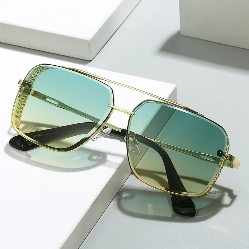 A pair of unique sunglasses with square gold metal frames and green gradient lenses offering UV protection, resting on a white and gray surface.