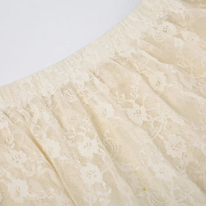 Close-up of a cream-colored silky lace fabric with a floral pattern, gathered with an elastic high waist.