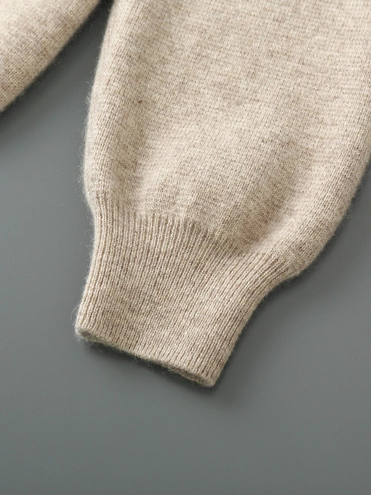 A close-up of the cuff and sleeve of a beige wool cardigan on a gray surface. The texture and ribbing of this autumn winter sweater are clearly visible, highlighting its cozy knit fabric.