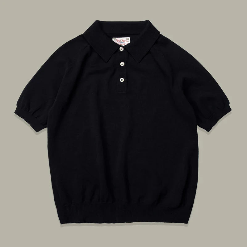 A classic style polo, this short-sleeve black knit mens polo shirt features a collar, three white buttons, ribbed cuffs, and a ribbed hem, laid flat on a neutral background.