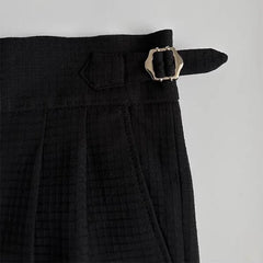 Close-up of the waistband of black luxury tailored pants with a silver buckle and strap detail on the side, set against a light background.