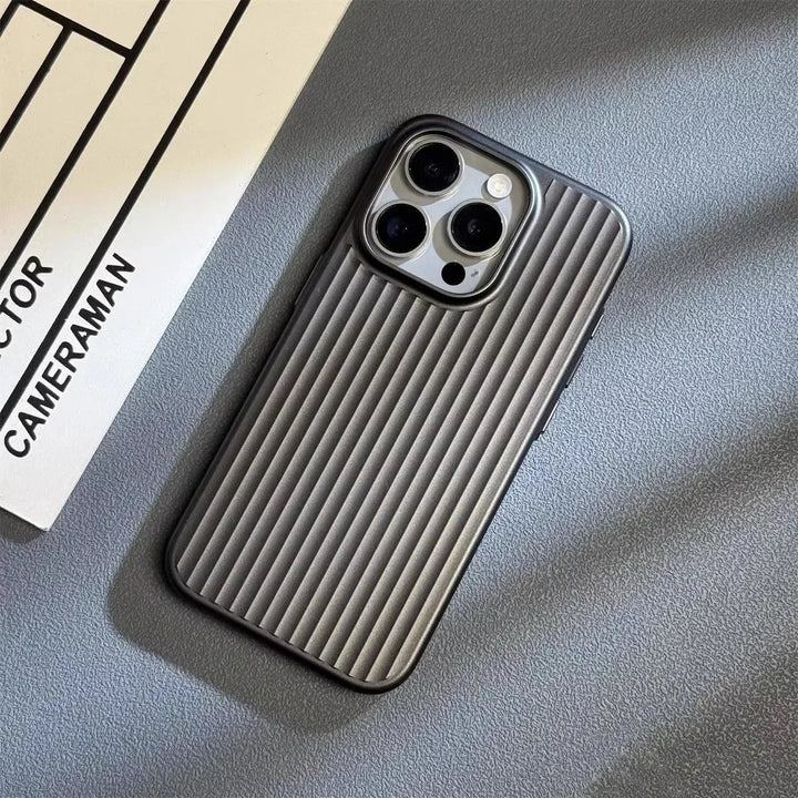 A smartphone with a slim lightweight design and ribbed gray case lies on a gray surface next to a white paper with the words CAMERAMAN and DIRECTOR partially visible. The phone’s three camera lenses are prominent.
