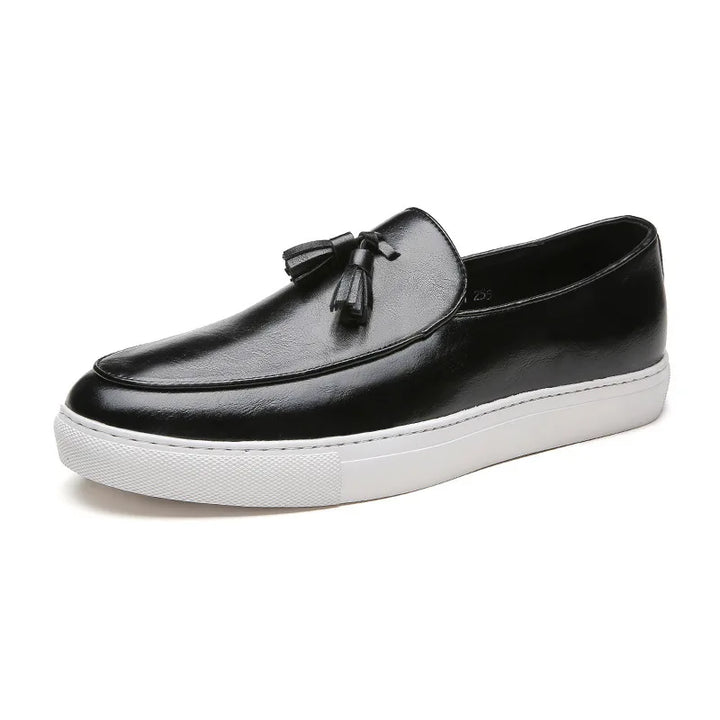 A luxury leather loafer with tassels on top and a thick white rubber sole, viewed from the side on a white background; these tassel loafers feature a cushioned insole for added comfort.