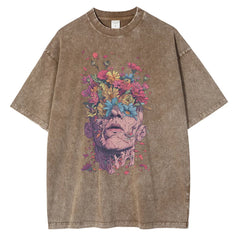 A brown, oversized fit T-shirt crafted from premium cotton, featuring a graphic design of a human head with vibrant flowers blooming from the top, blending surreal and botanical elements across the chest.