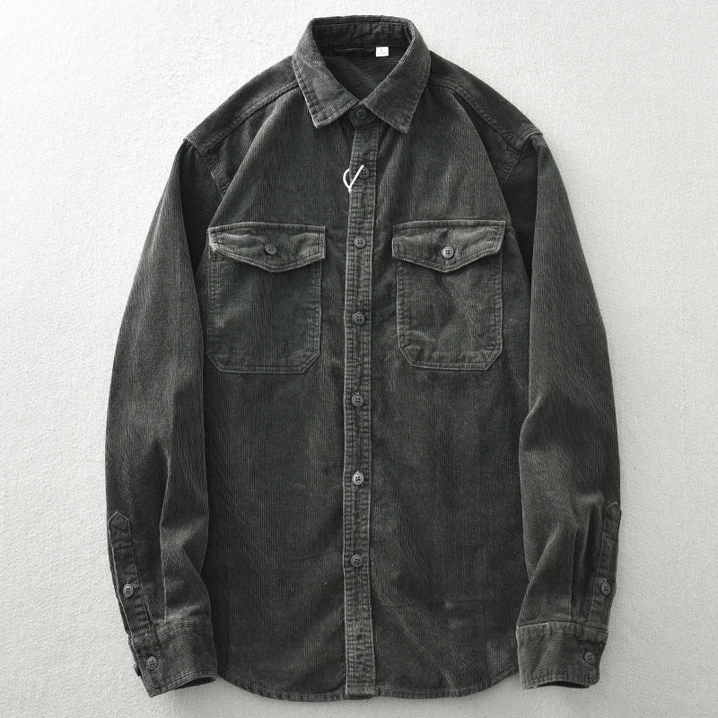 A dark gray, heavyweight cotton button-up shirt with corduroy detailing, long sleeves, a collar, and two chest pockets, laid flat on a light-colored surface.