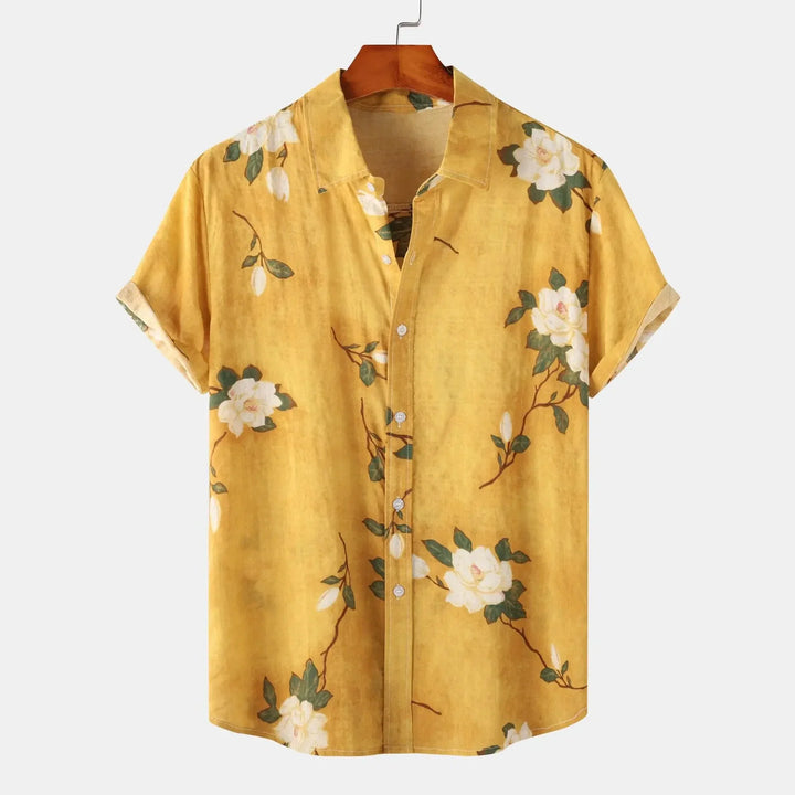 A short-sleeved, button-up yellow linen shirt with a collar, featuring a white floral and green leaf pattern, displayed on a wooden hanger against a plain background—perfect for effortless summer style.