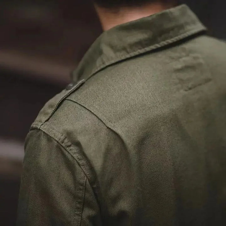 Close-up view of the back and shoulder of a person wearing an olive green collared tactical jacket, focusing on the fabric texture and precise stitching details.