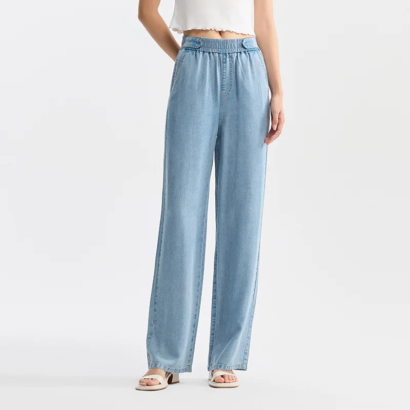 A person wearing light blue, wide-leg jeans crafted from breathable denim with an elastic waistband, a white cropped top, and sandals, standing against a plain white background.