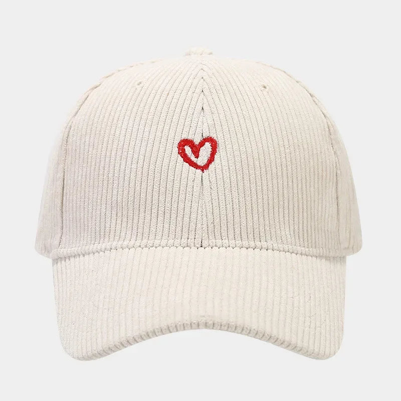 A beige corduroy hat with a FlexFit band, featuring a small red heart embroidery on the front center. The background is plain white.