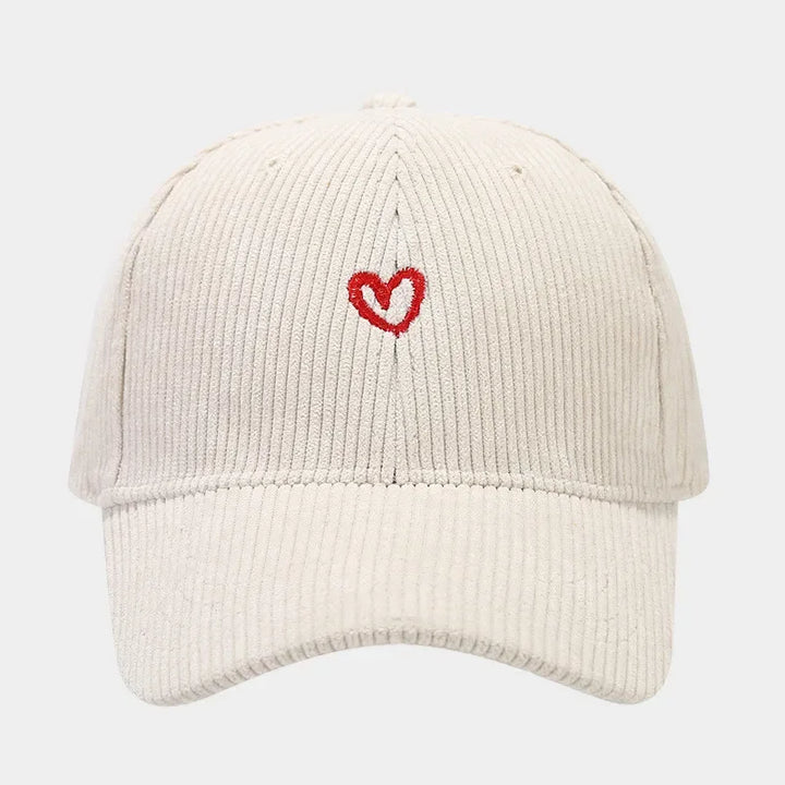 A beige corduroy hat with a FlexFit band, featuring a small red heart embroidery on the front center. The background is plain white.