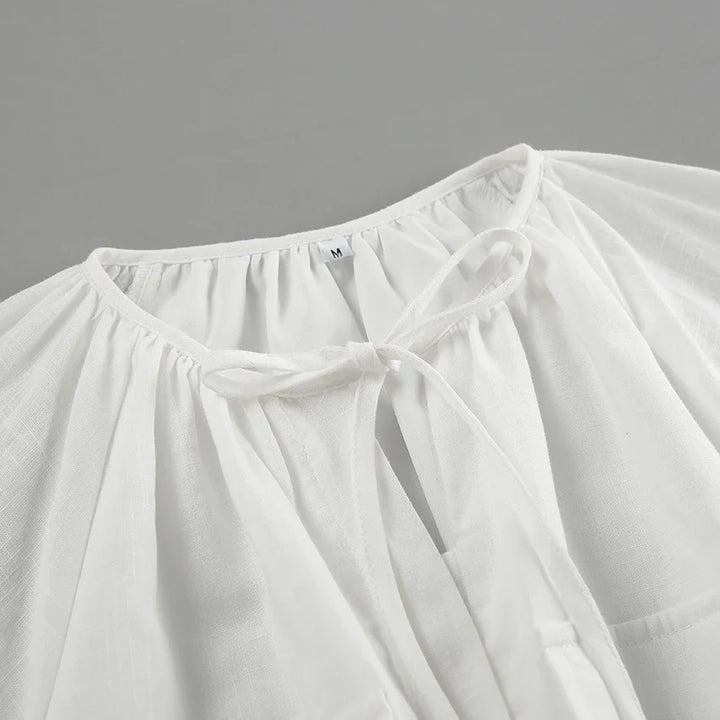 A close-up of the neckline of a white, lightweight, long-sleeve blouse with a drawstring tie at the collar—perfect for a summer outing. The slightly sheer fabric is gathered around the neckline, and a size M tag is visible inside.