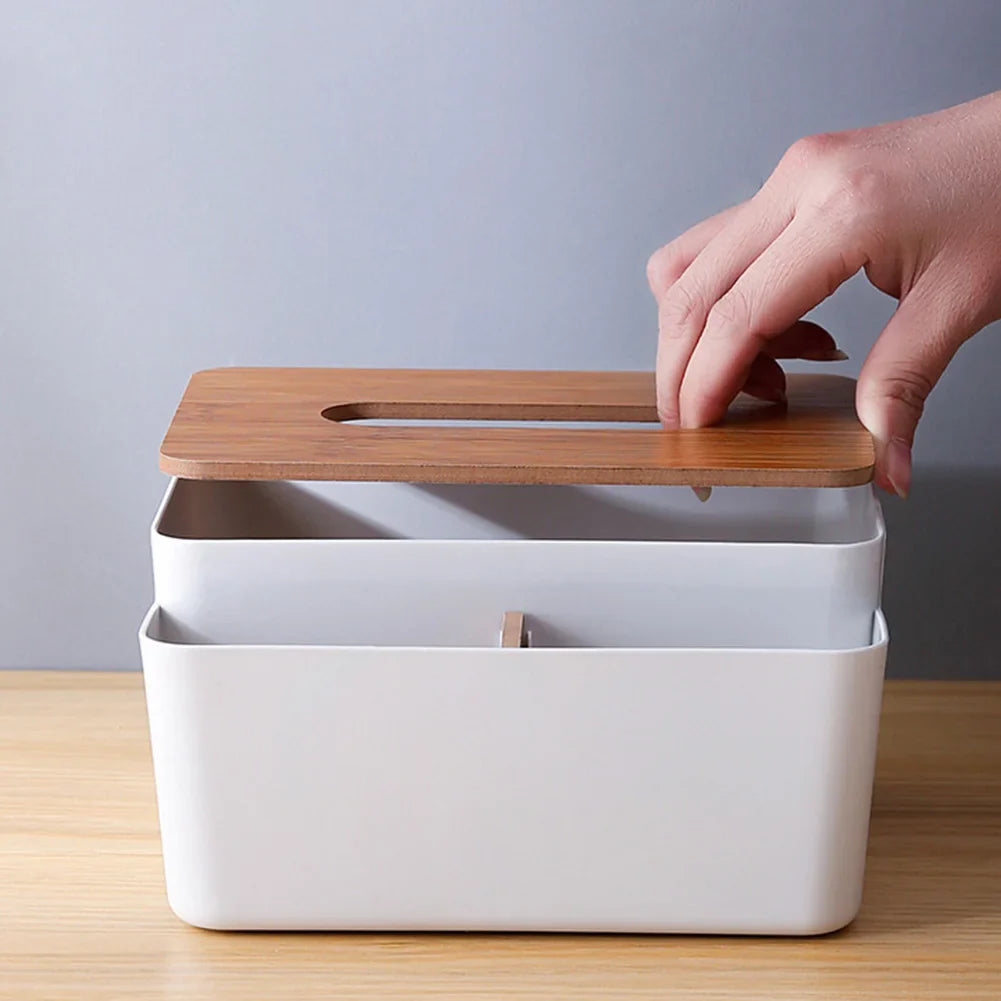 A hand lifts the wooden lid of a rectangular Table Wooden Cover Tissue Box with a slot, placed on a light wooden surface against a gray background.
