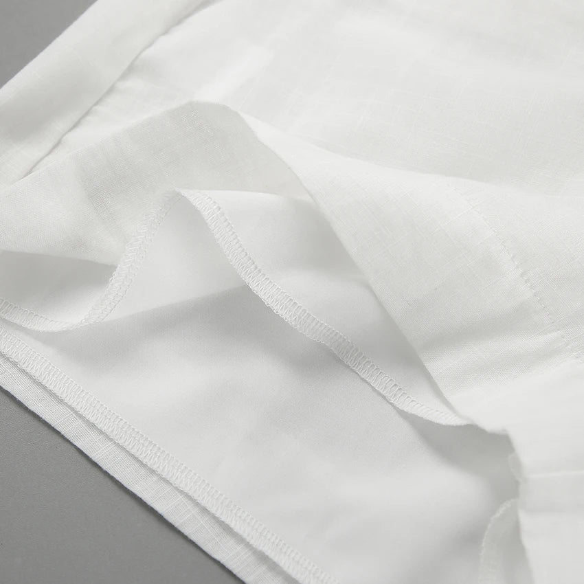 Close-up of a chic romper’s white fabric with neatly sewn hems and seams, showing layered edges and fine stitching, placed on a flat gray surface.