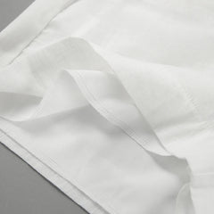 Close-up of a chic romper’s white fabric with neatly sewn hems and seams, showing layered edges and fine stitching, placed on a flat gray surface.