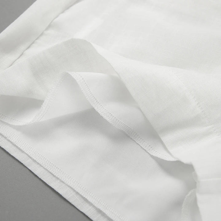 Close-up of a chic romper’s white fabric with neatly sewn hems and seams, showing layered edges and fine stitching, placed on a flat gray surface.