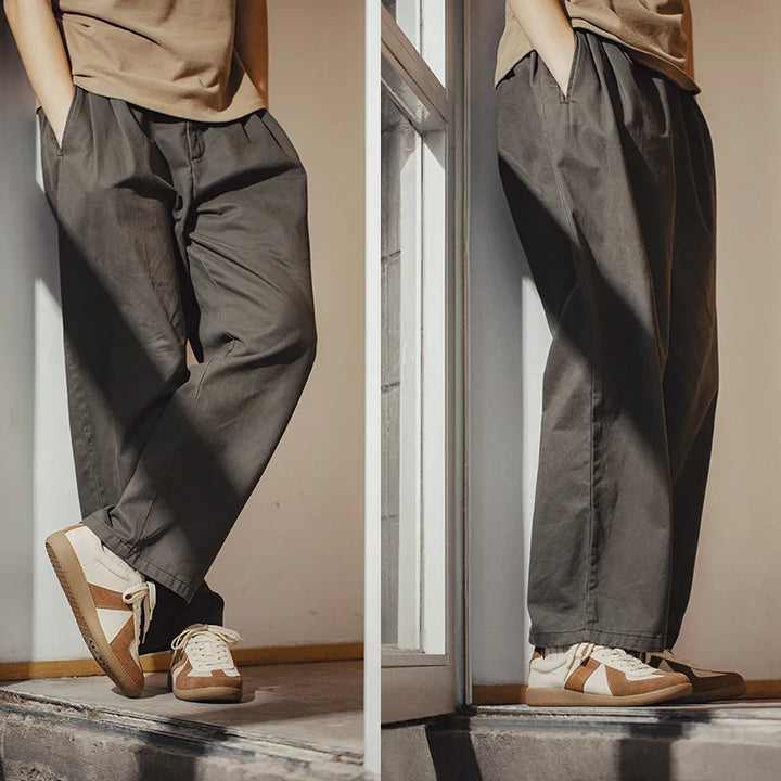 Two side-by-side photos show a person wearing loose-fitting dark gray pants, a beige shirt, and lightweight breathable sneakers with EVA midsole cushioning. The beige sneakers with white soles add comfort as they stand indoors by the window, hands in pockets.