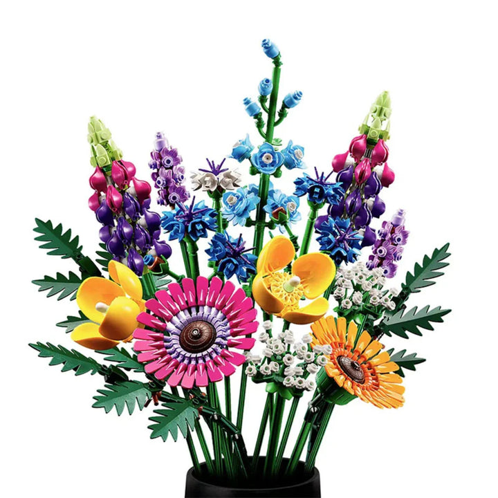 A colorful bouquet of flowers made from LEGO building blocks, featuring pink, purple, yellow, orange, and blue blossoms with green leaves, arranged in a black vase on a white background.