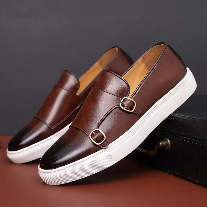 A pair of brown Men's Casual Leather Shoes with double buckle detailing and white rubber soles, these Slip-On Loafers showcase classic British Fashion against a dark background.