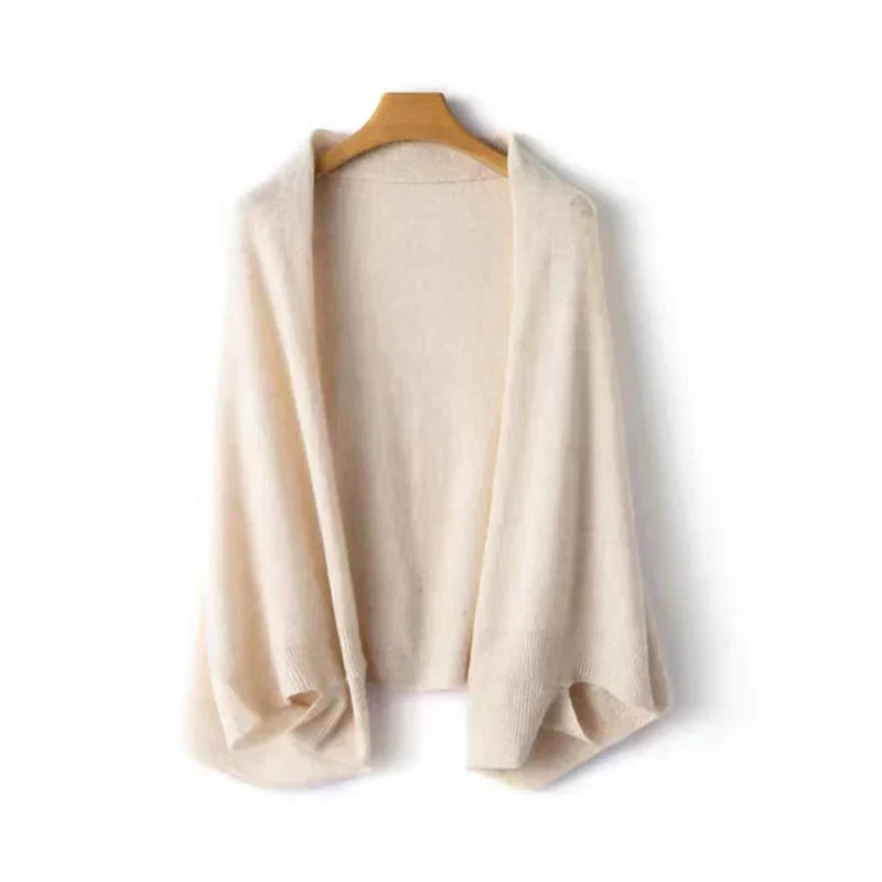 A cream-colored, open-front knit cardigan with draped lapels, crafted in a soft cashmere blend for cozy autumn winter layering, hangs on a wooden hanger against a white background.