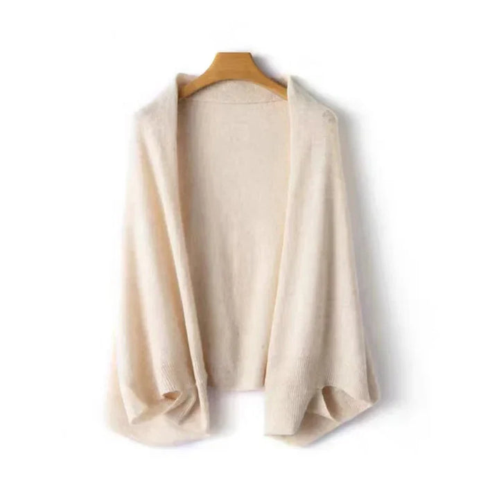 A cream-colored, open-front knit cardigan with draped lapels, crafted in a soft cashmere blend for cozy autumn winter layering, hangs on a wooden hanger against a white background.