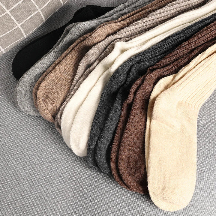 Several pairs of socks in neutral tones—black, gray, brown, beige, and cream—are neatly arranged side by side on a light gray fabric surface, showcasing breathable socks in a premium Cashmere cotton blend.