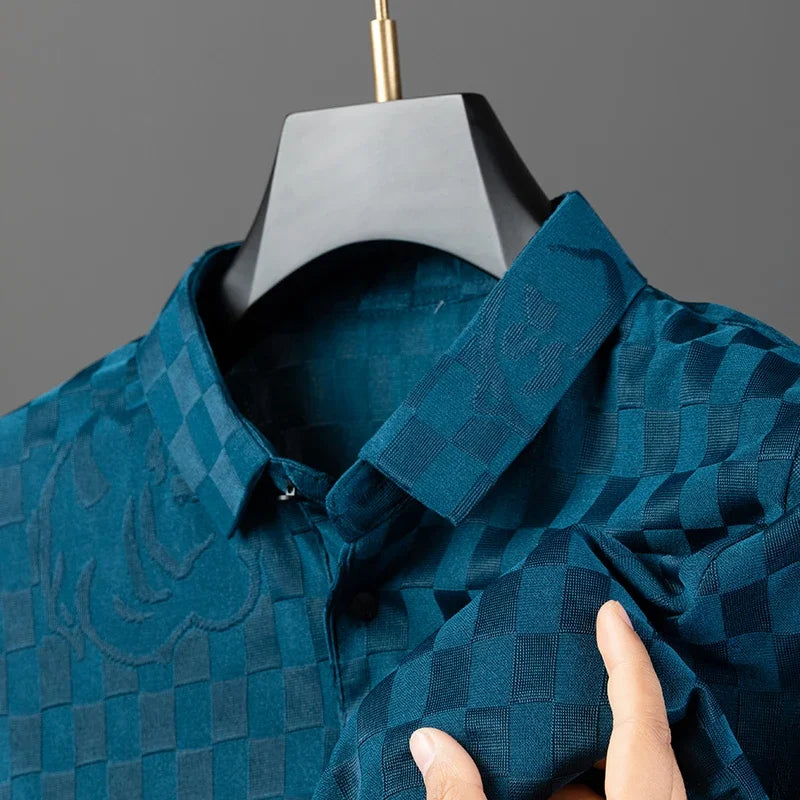 A hand holds the sleeve of a blue, tailored fit button-up shirt with subtle textured patterns and a checkerboard pattern, displayed on a black hanger against a gray background.